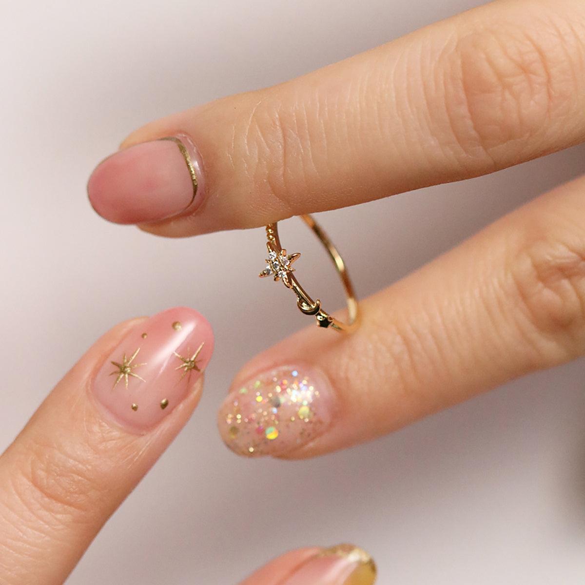 Elegant moon and star ring held between fingers with stylish nail art, showcasing celestial beauty and intricate design.