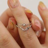 Close-up of two dainty silver rings with floral designs, worn on a hand with pastel nail art.